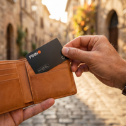 PINNO tracking card sliding into a leather wallet on a sunlit European street